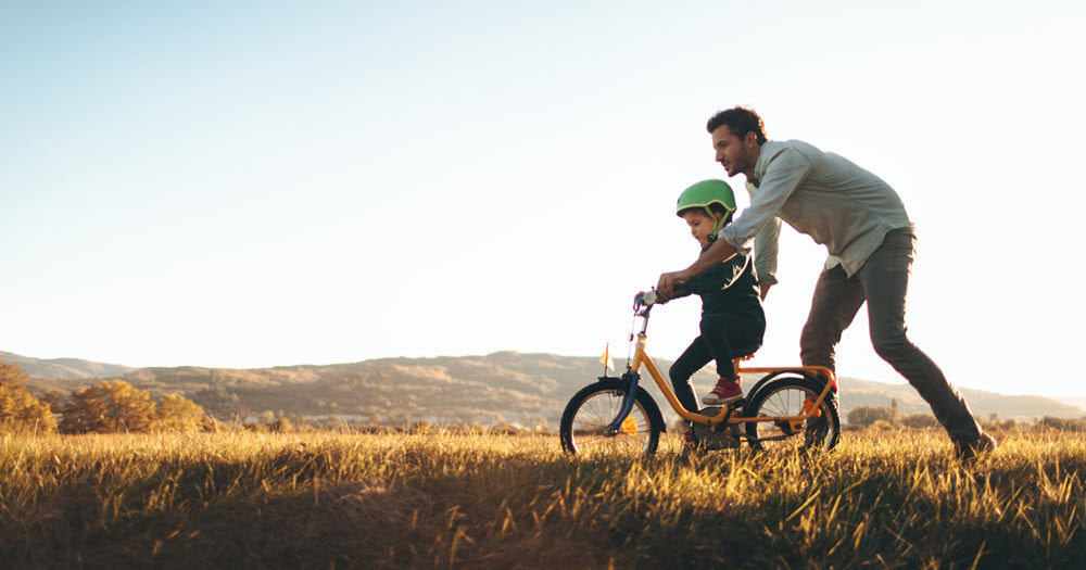 Father teaching son to ride a bicycle.