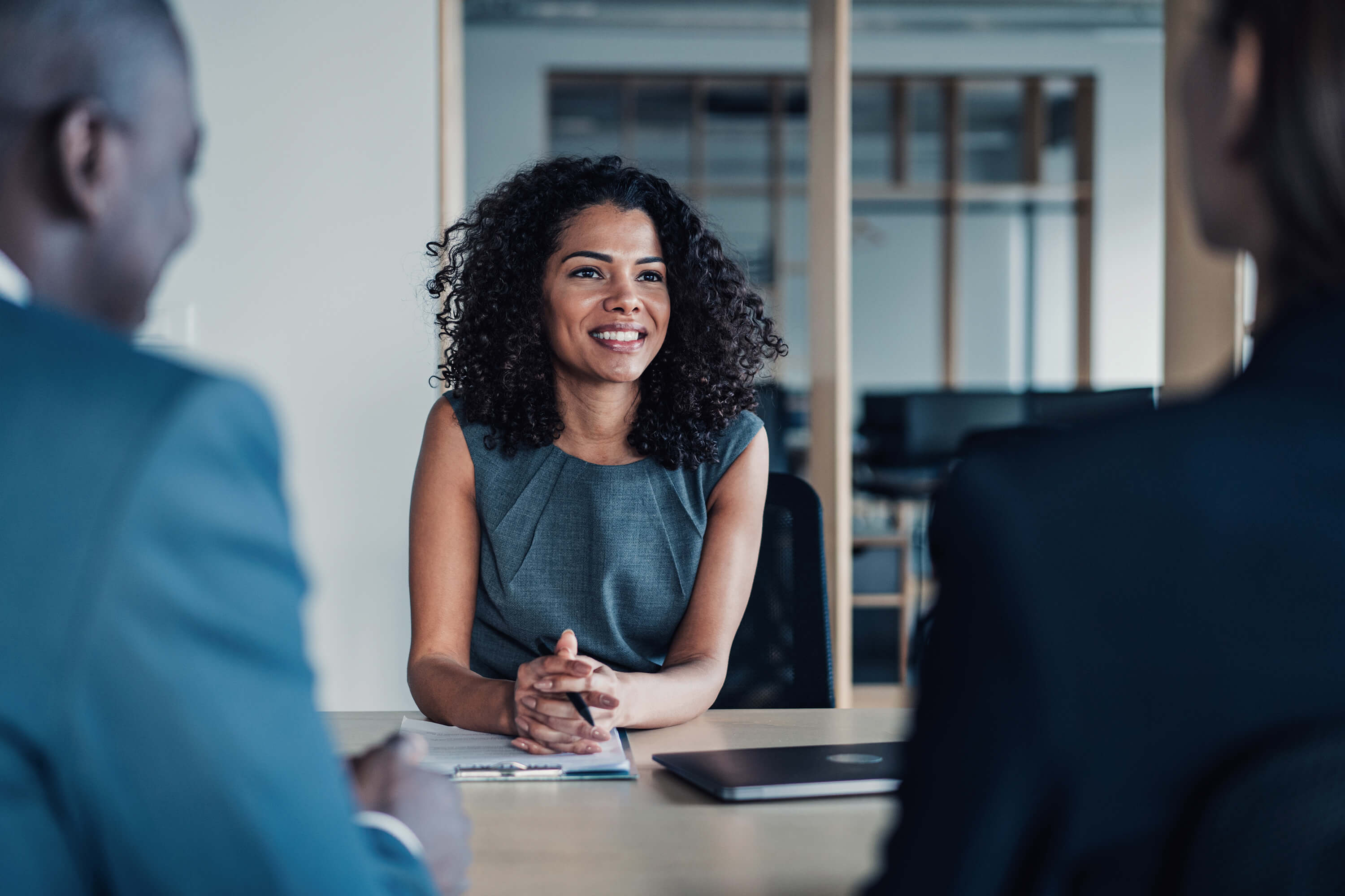 Woman at desk with pen  and clipboard smiling across the table