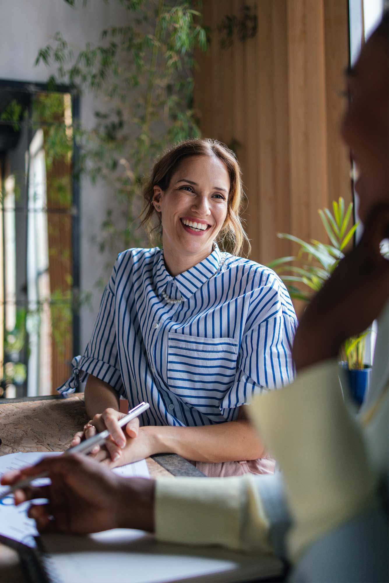 Close up of a happy businesswoman sitting at the table in the office, smiling and looking at her female colleague.  