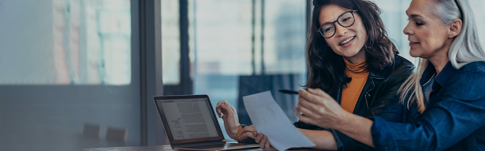 Two women analyzing documents while sitting at a table in an office.