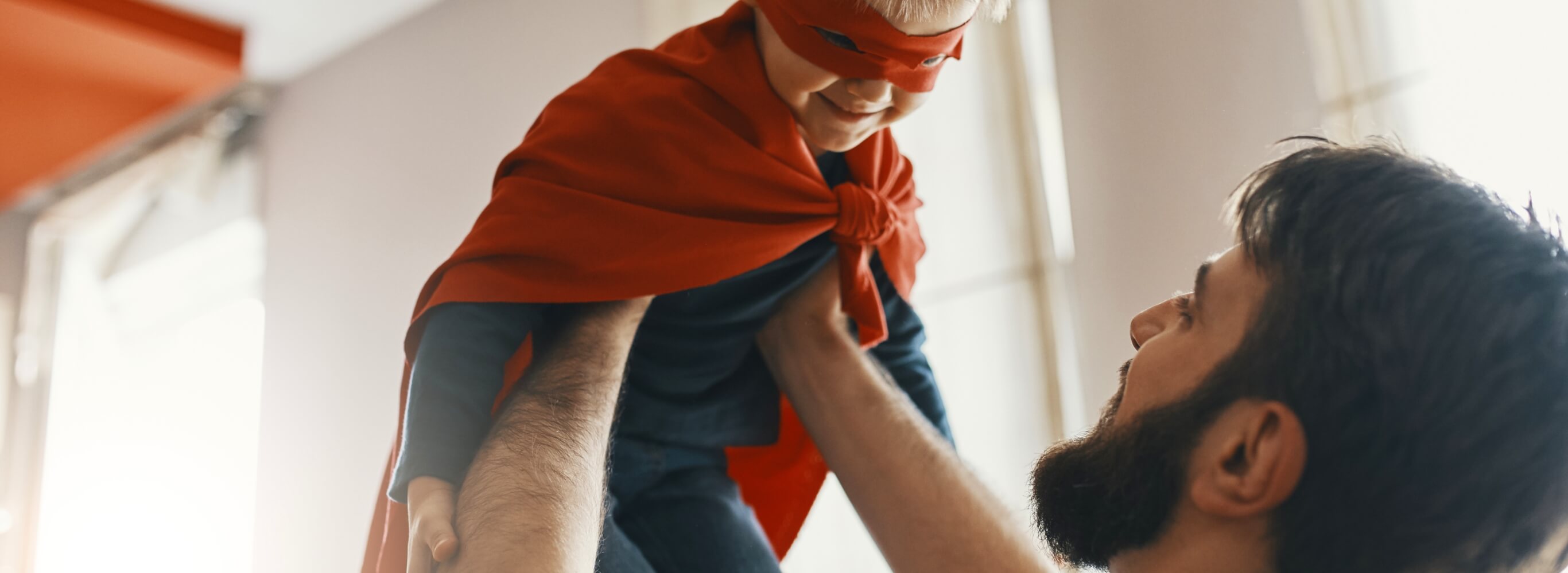 Man holding up his son, dressed as a superhero.