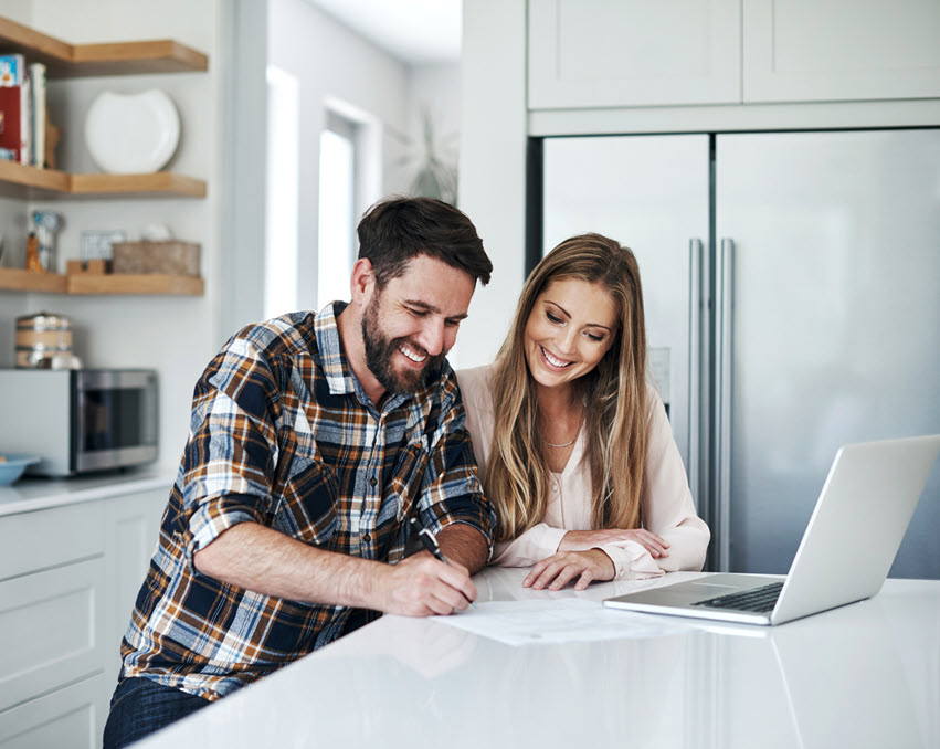 couple filling out paperwork with open laptop on countertop
