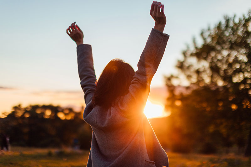 Woman with victorious arms up in front of sunset.