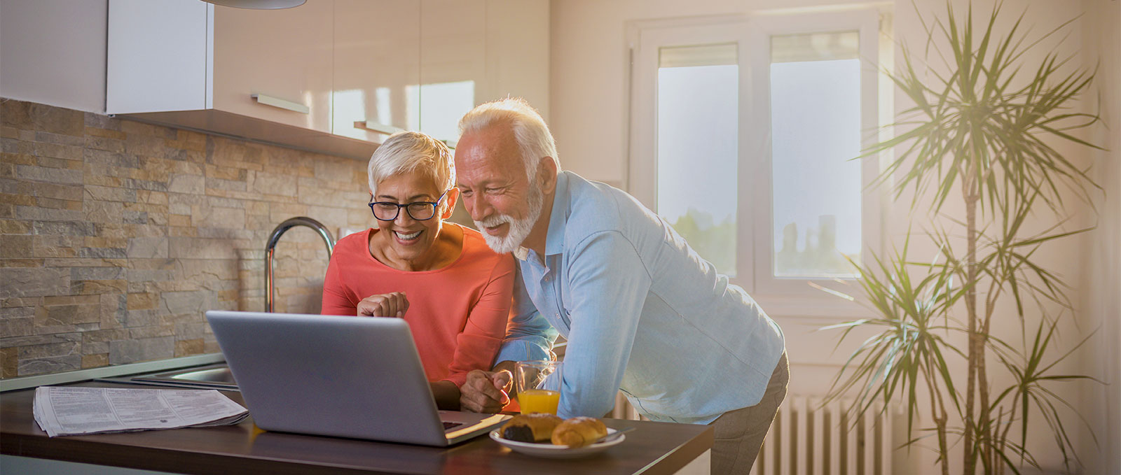 Mature couple staying using their laptop in their kitchen.