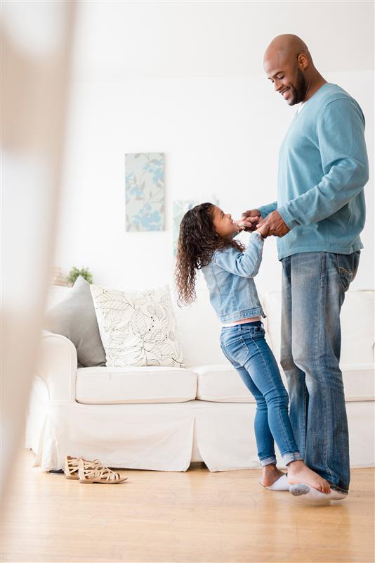 Smiling aughter standing on feet of father in their living room.